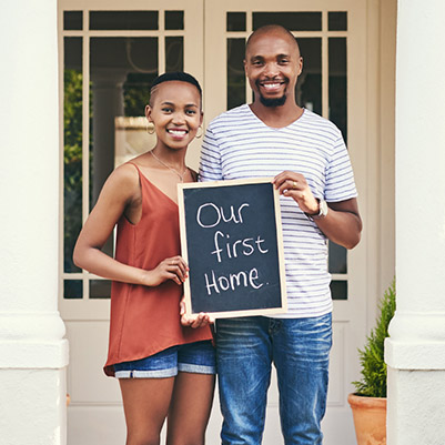 Photo of a couple holding a sign that says 'our first home'